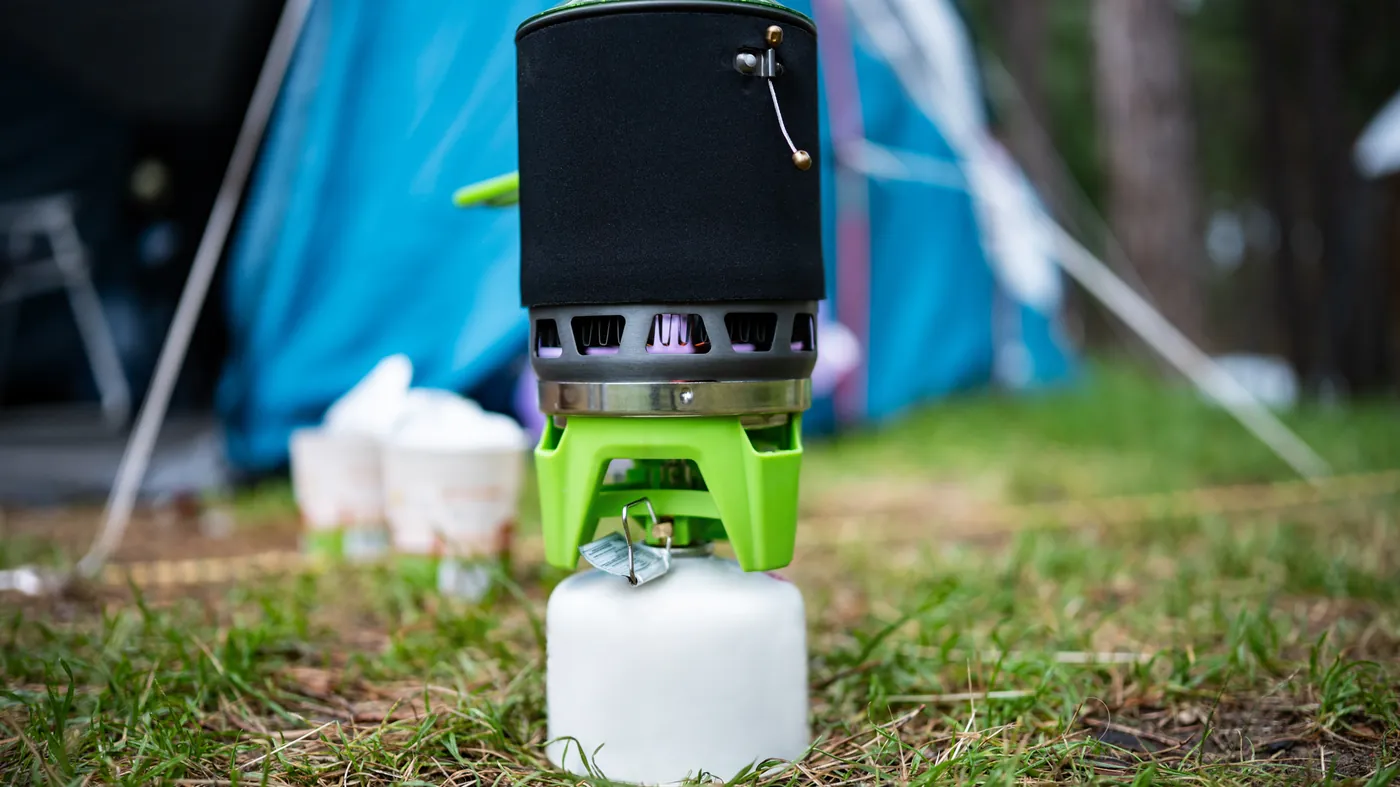 A camping gas stove boiling water beside a tent