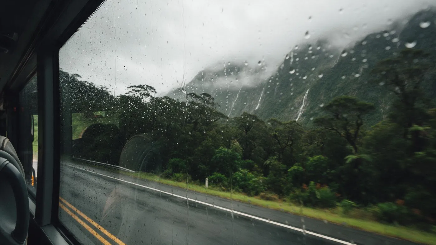 Regen auf einem Busfenster an einer nassen Bergstraße durch den Wald