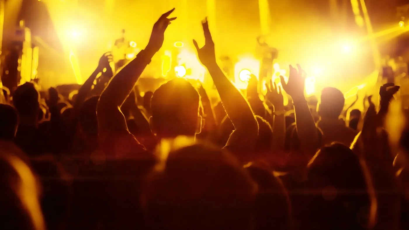 Concertgoers with raised hands in front of a stage in warm light