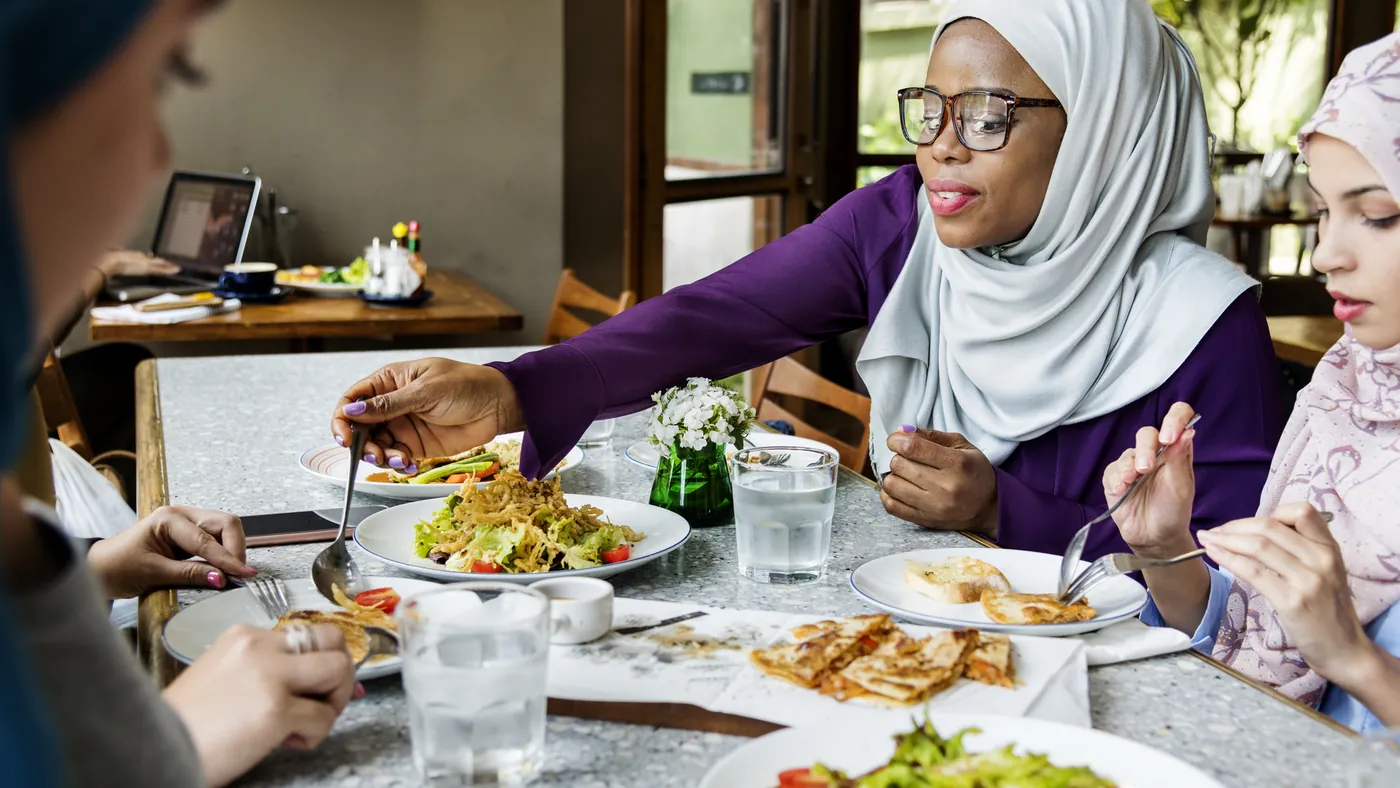 Friends in headscarves sharing a meal at a restaurant table