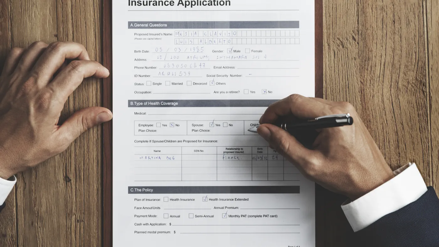 Hands filling in an insurance application form on a wooden table