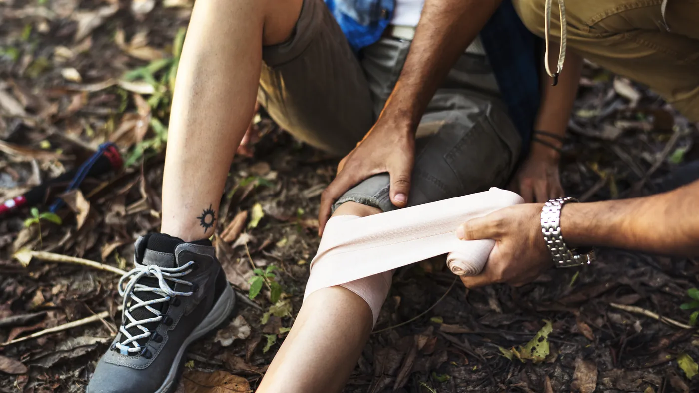 A hiker's knee being bandaged on a forest floor