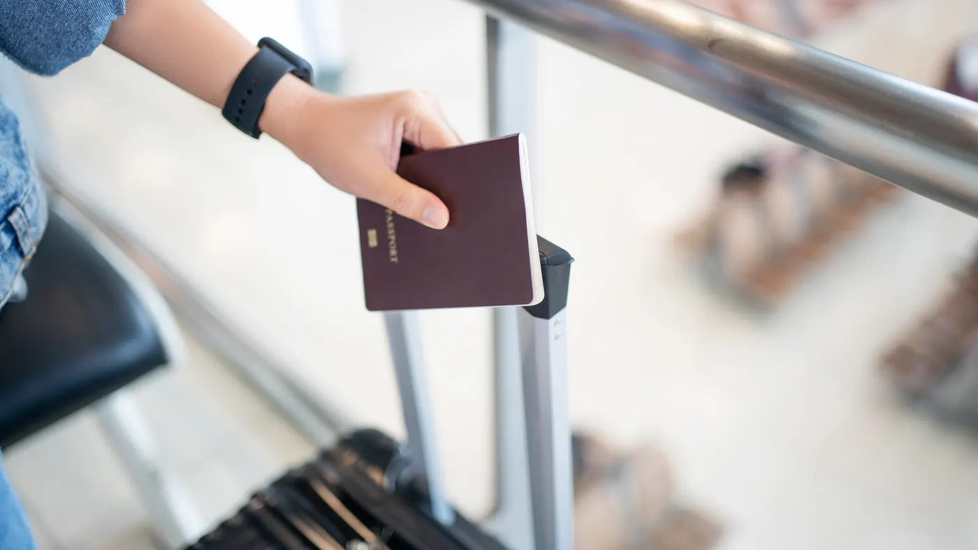 A hand holding a passport above a suitcase handle