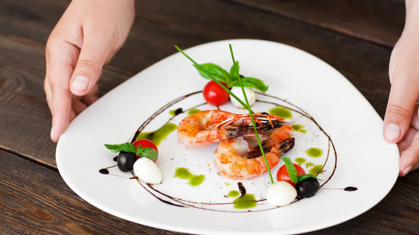 A plate of prawns with tomato and herbs being set down on a dark wooden table
