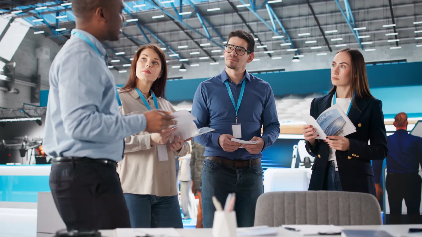 Four delegates with name badges reading brochures at an exhibition stand