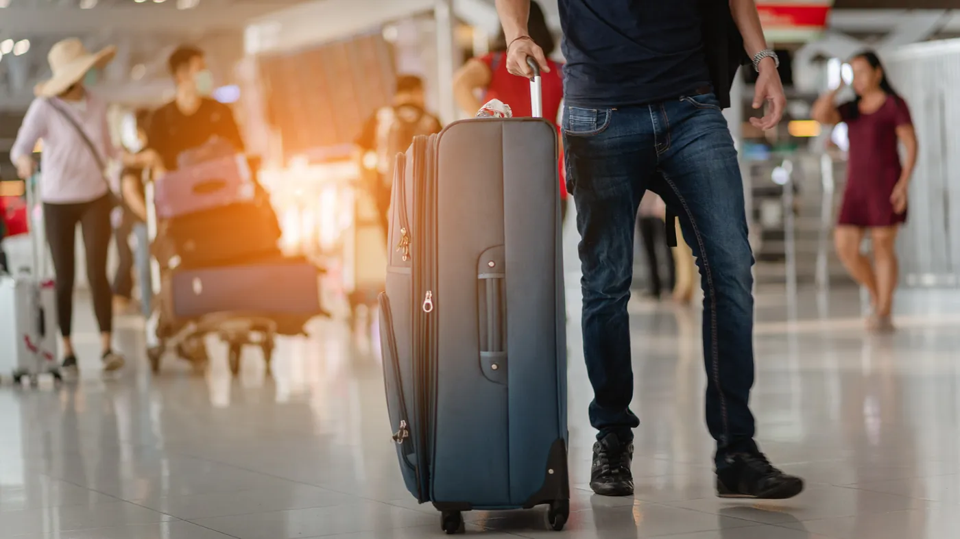 Travellers wheeling suitcases through a bright airport terminal
