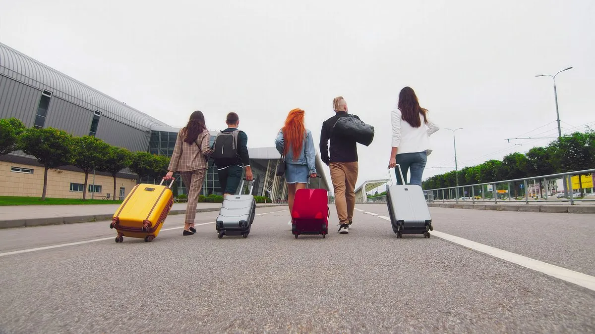 A group of travellers wheeling suitcases along a path outside an airport terminal