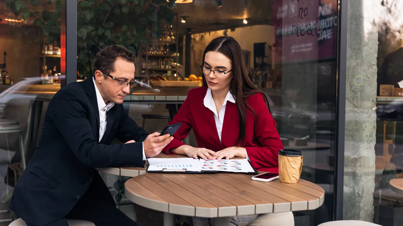 Two people at a café table looking at a brochure and a phone