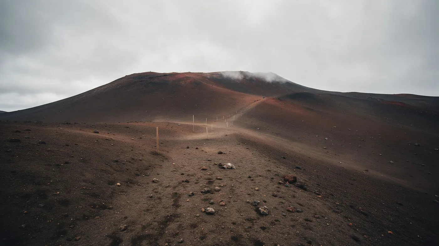A poled route across a bare volcanic plateau under low cloud