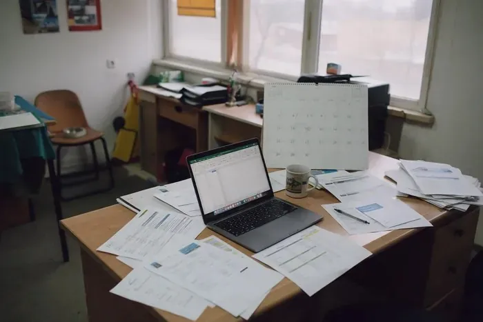 Papers and a laptop on a desk below a wall calendar