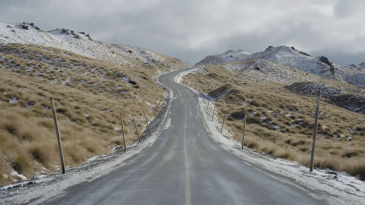 A sealed road winding through snowy tussock high country