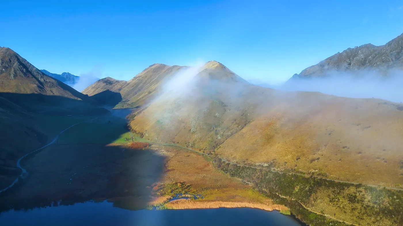 Fog rolling over sunlit mountains near Moke Lake, seen from the air