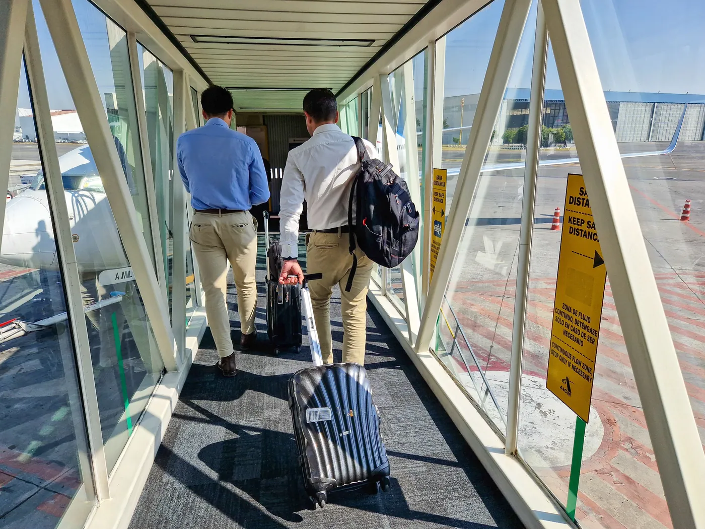 Two travellers wheeling suitcases along an air bridge to a plane
