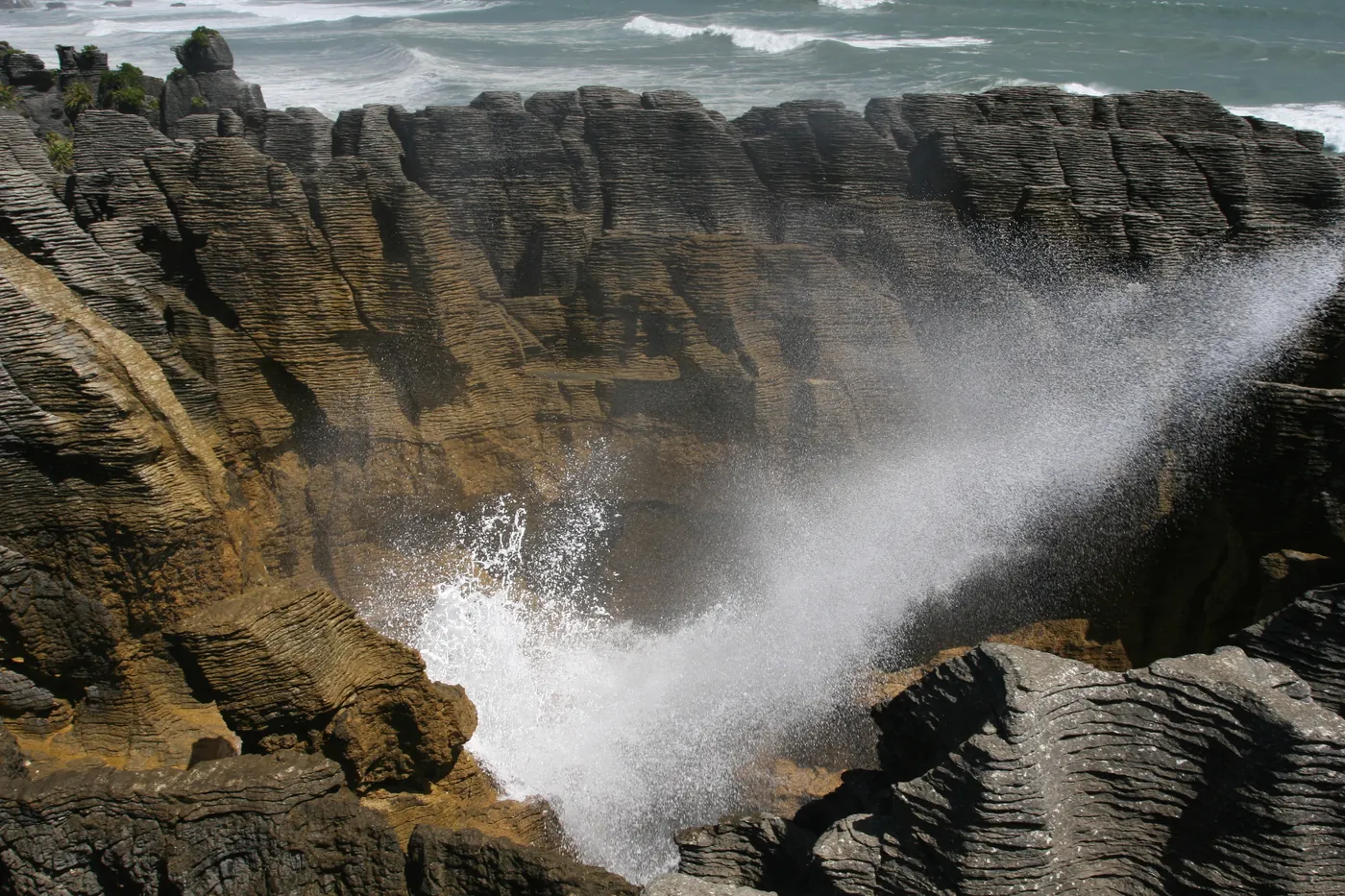 Pancake Rocks at Punakaiki, with spray bursting from a blowhole between layered limestone rocks