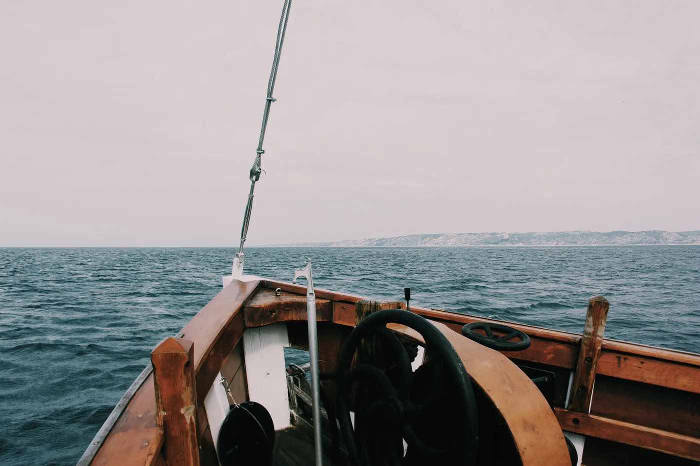 The bow of a wooden boat heading out across open water towards a low coastline