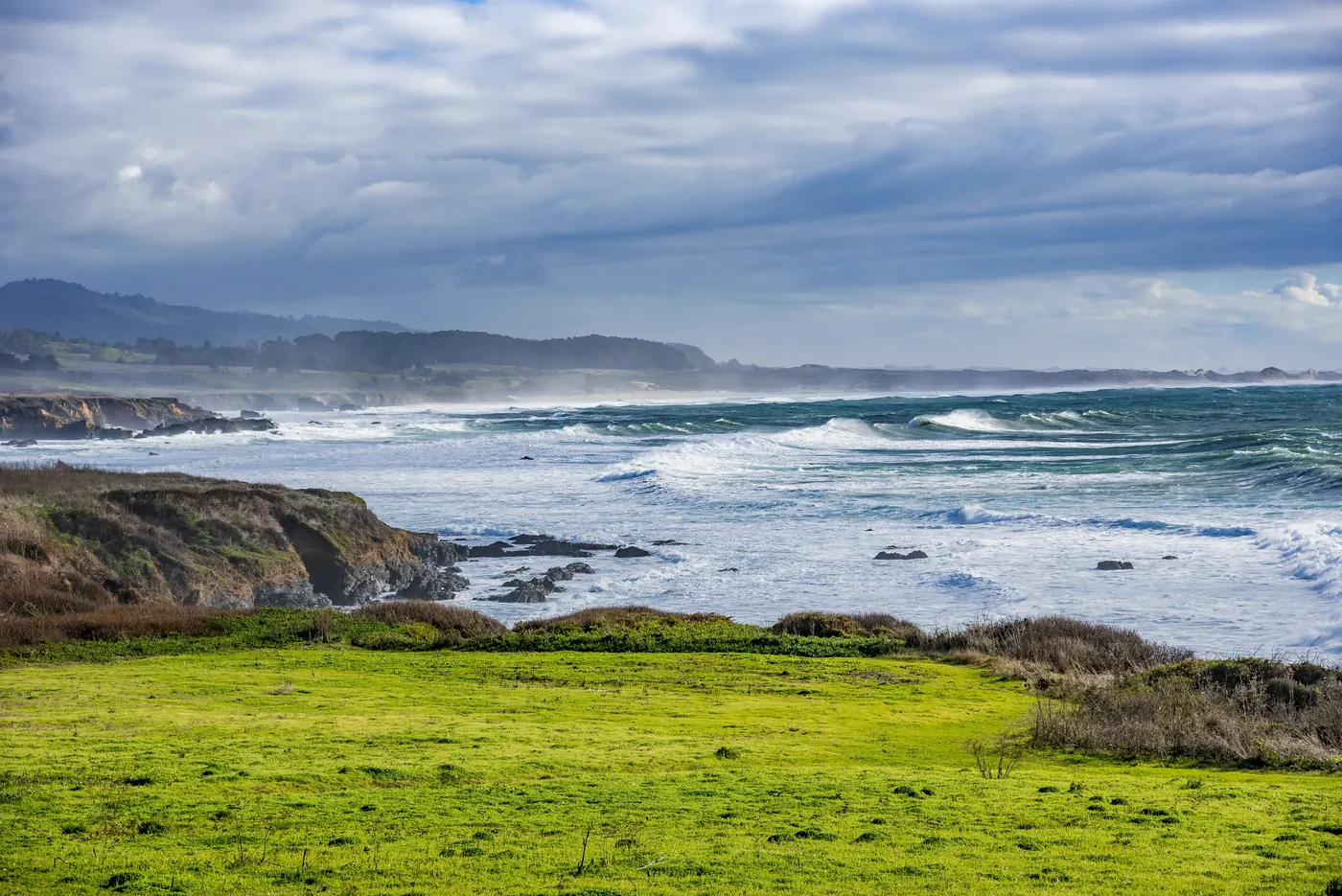 Rough surf breaking on a rocky coast beyond green pasture