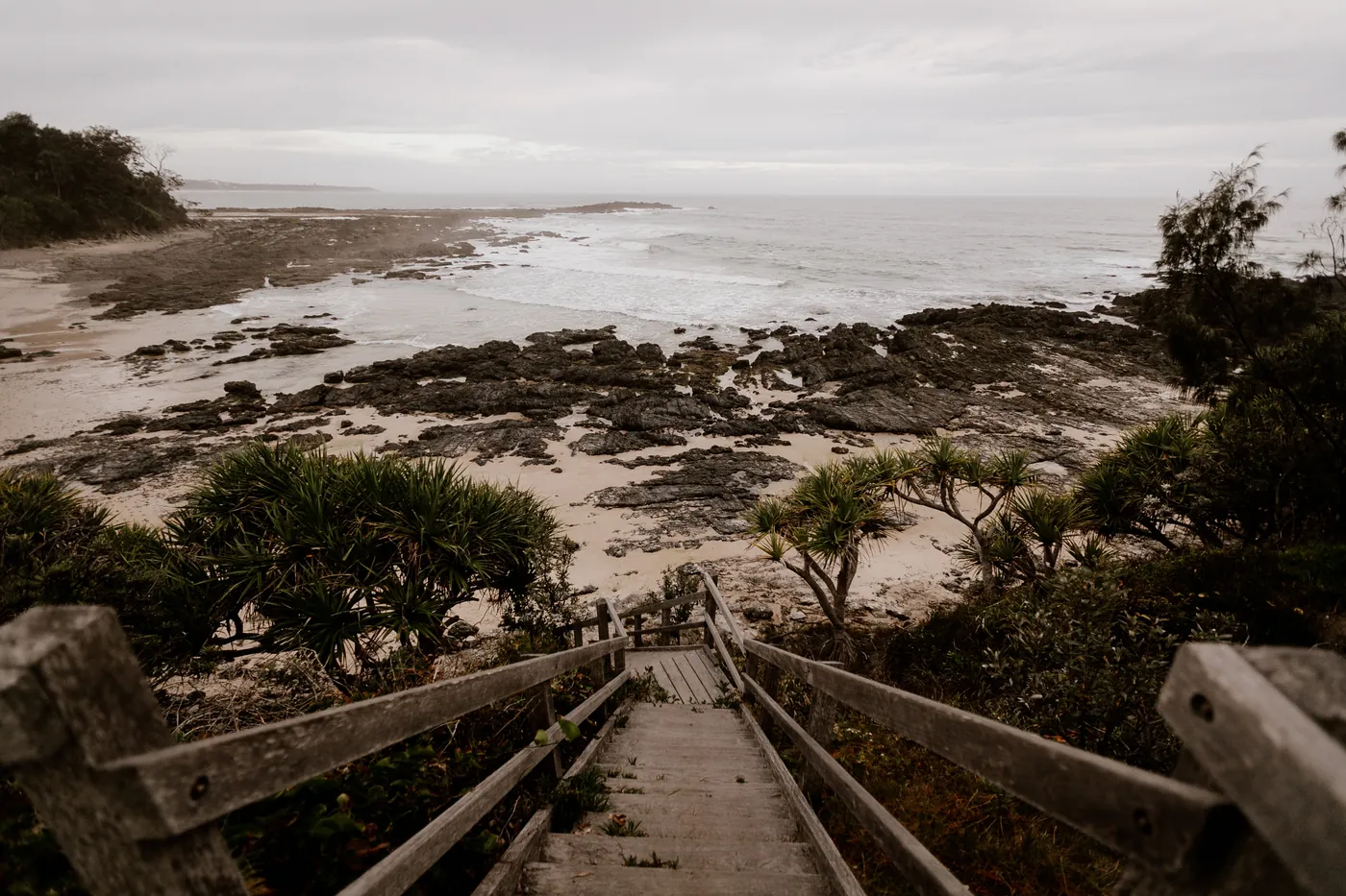 Wooden steps leading down to a rocky shore under a grey sky