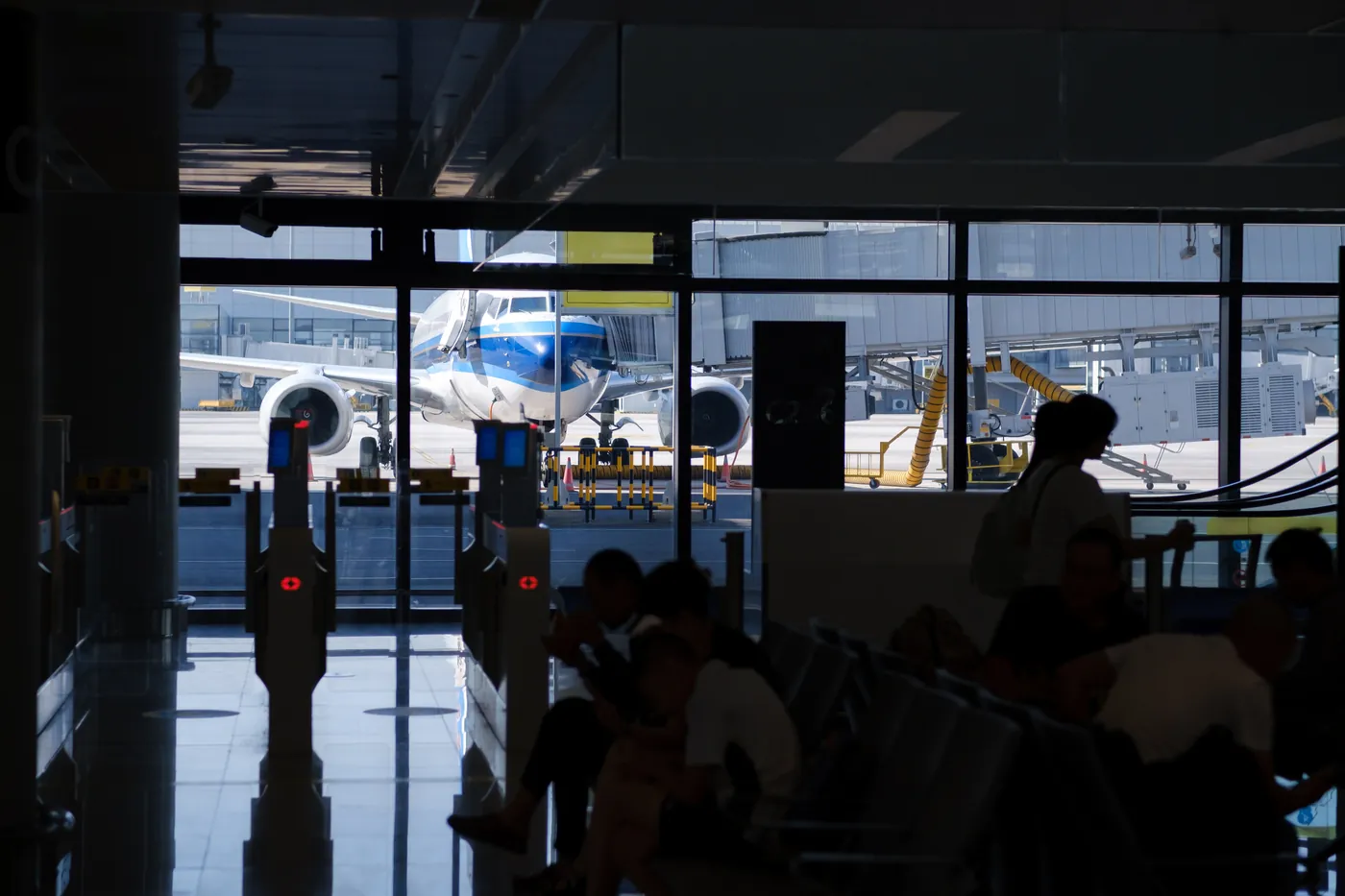 Passengers waiting in a terminal while a jet stands outside the windows