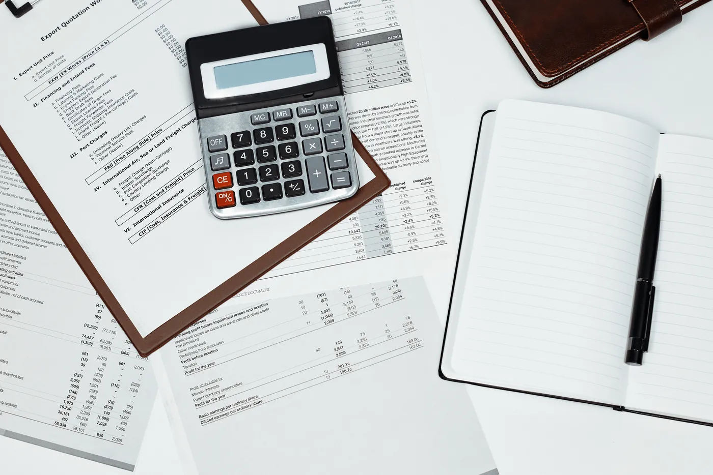 A calculator on a clipboard of printed figures beside an open notebook