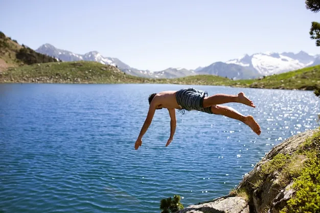 A swimmer leaping into a mountain lake below rocky peaks