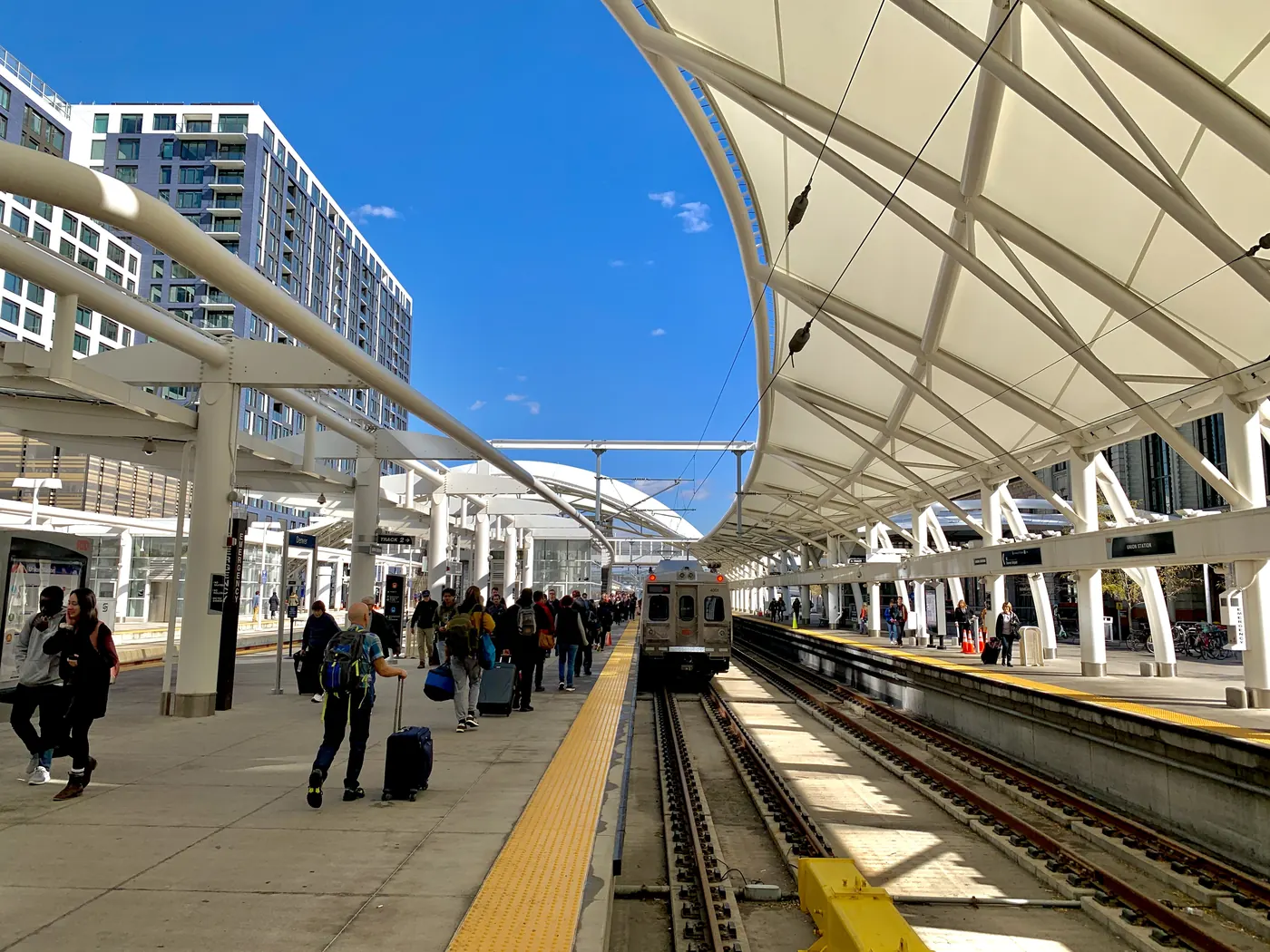 Travellers with suitcases on a sunlit rail platform