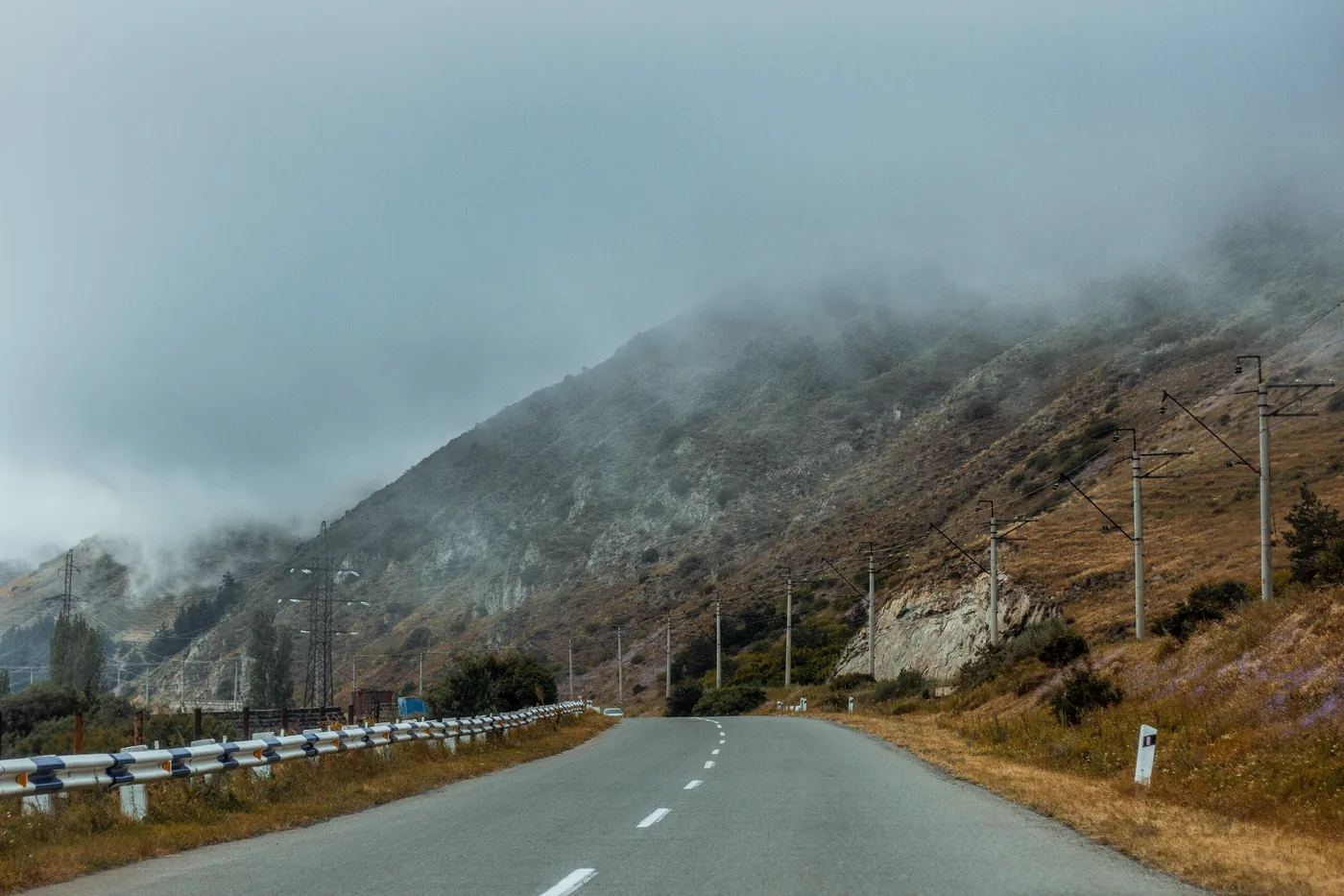 A road below high mountains wrapped in fog