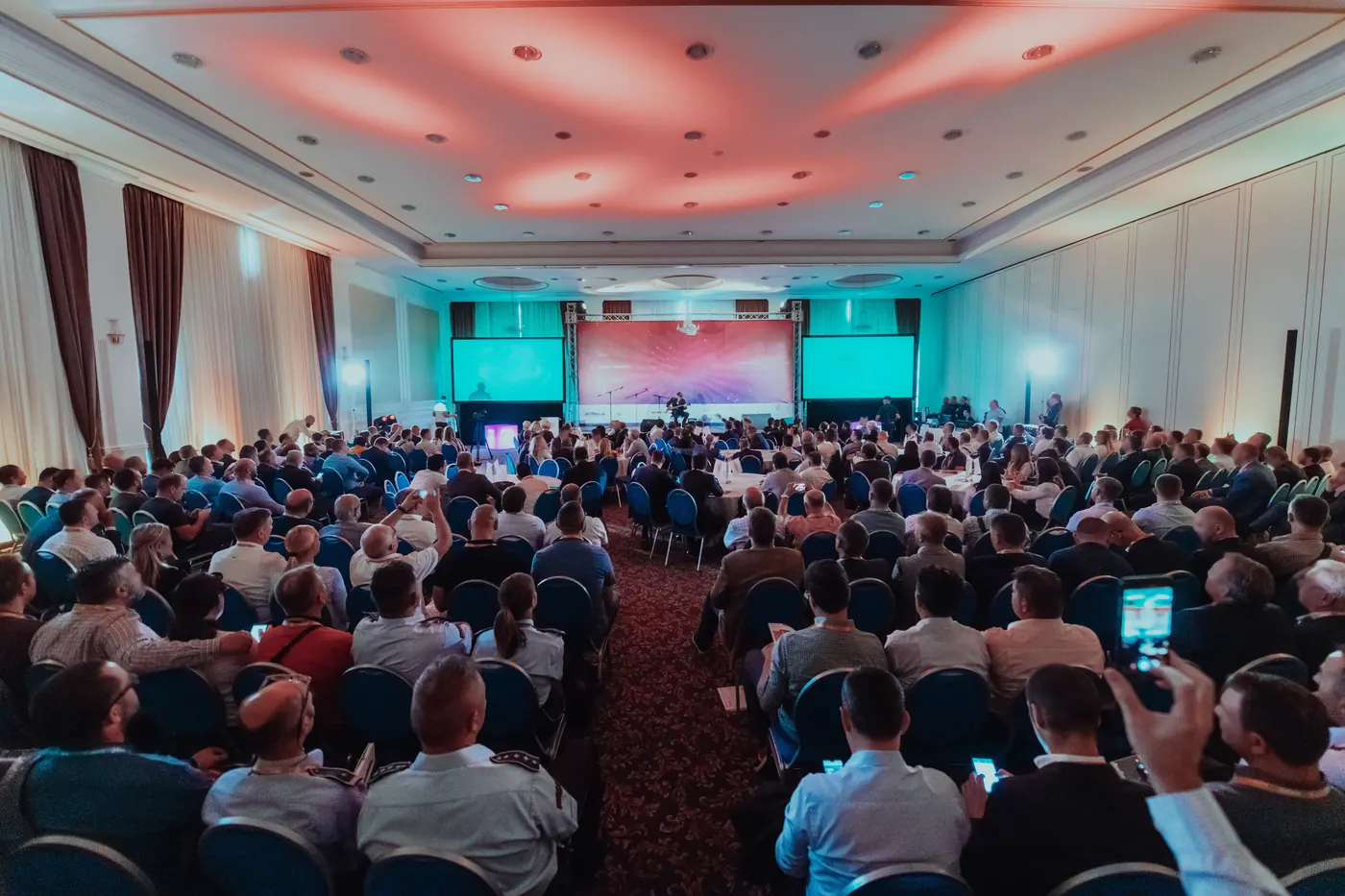 A full conference hall facing a stage and screens
