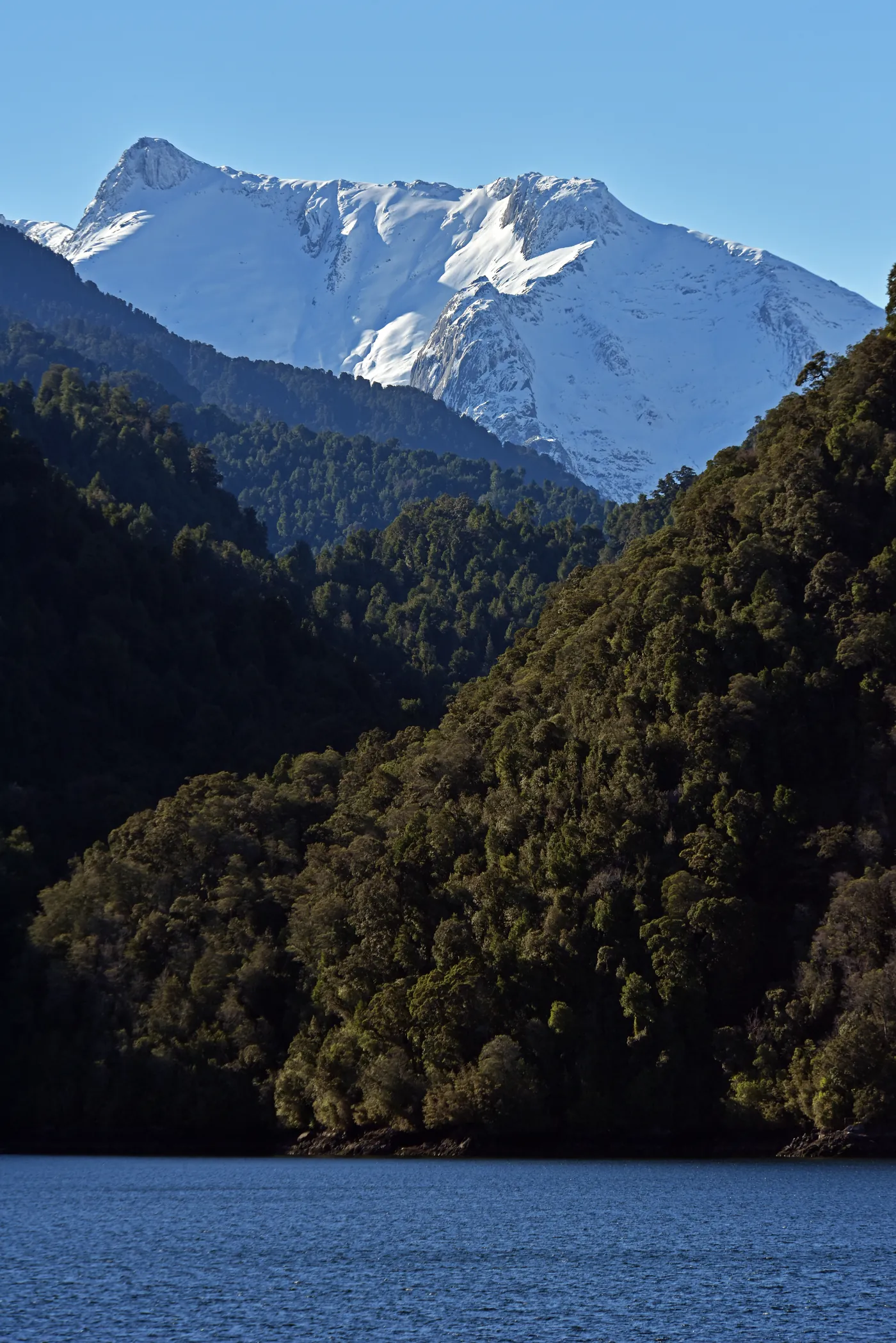 Snow-capped peaks above forested slopes and a deep blue lake