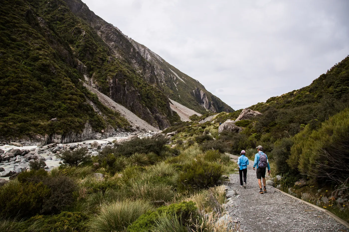 Two walkers on a gravel track in a steep mountain valley