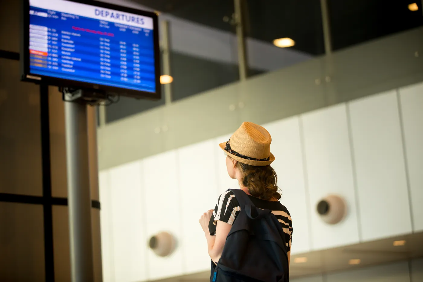 A traveller in a sun hat looking up at an airport departures screen